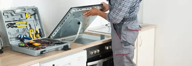 Cooktop repair technician lifting a built-in stovetop for service in Nashville, TN
