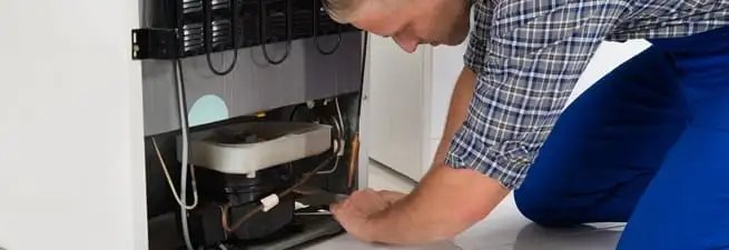 Refrigerator repair technician servicing the compressor and condenser area in Nashville, TN