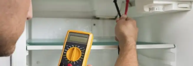 Refrigerator repair technician testing electrical components with a multimeter in Nashville, TN